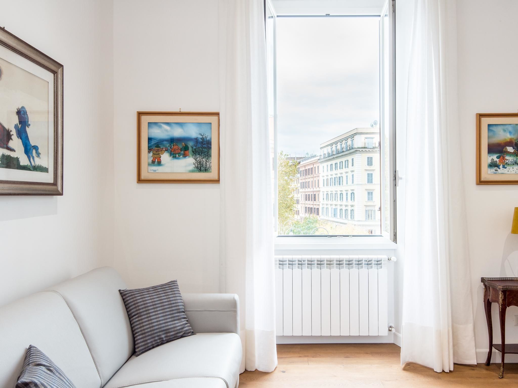 A living room with a white sofa, a radiator, and a window with a view of buildings.