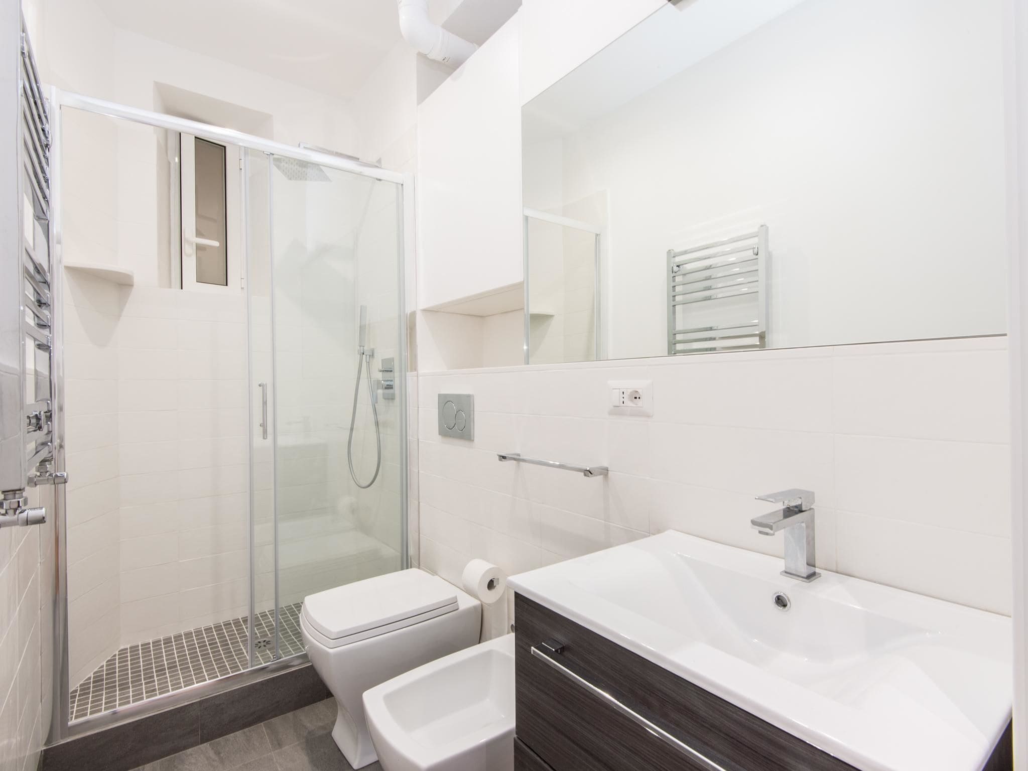 Et moderne badeværelse med en glasafskærmet brusekabine, et hvidt toilet, en vaskebord med vask og et spejl.