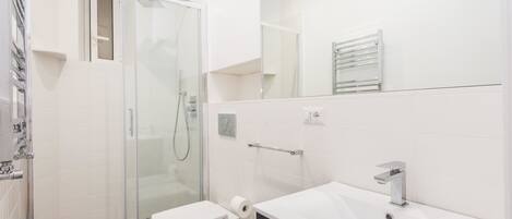 Et moderne badeværelse med en glasafskærmet brusekabine, et hvidt toilet, en vaskebord med vask og et spejl.