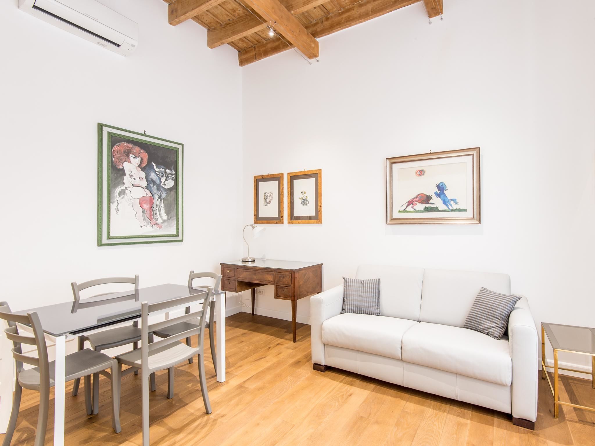 A room with a wooden ceiling, a white sofa, a dining table with chairs, and framed artwork on the walls.