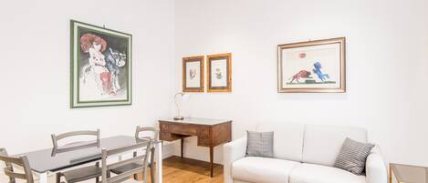 Une pièce avec un plafond en bois, un canapé blanc, une table à manger avec des chaises et des œuvres d’art encadrées accrochées aux murs.