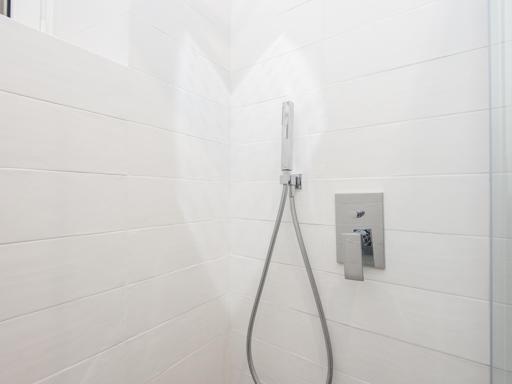 A shower area with white tiled walls and a chrome showerhead.