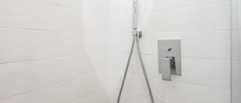 A shower area with white tiled walls and a chrome showerhead.