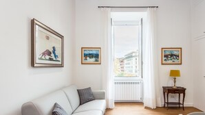 A modern living room with a sofa, a small table with a lamp, and a window with curtains.