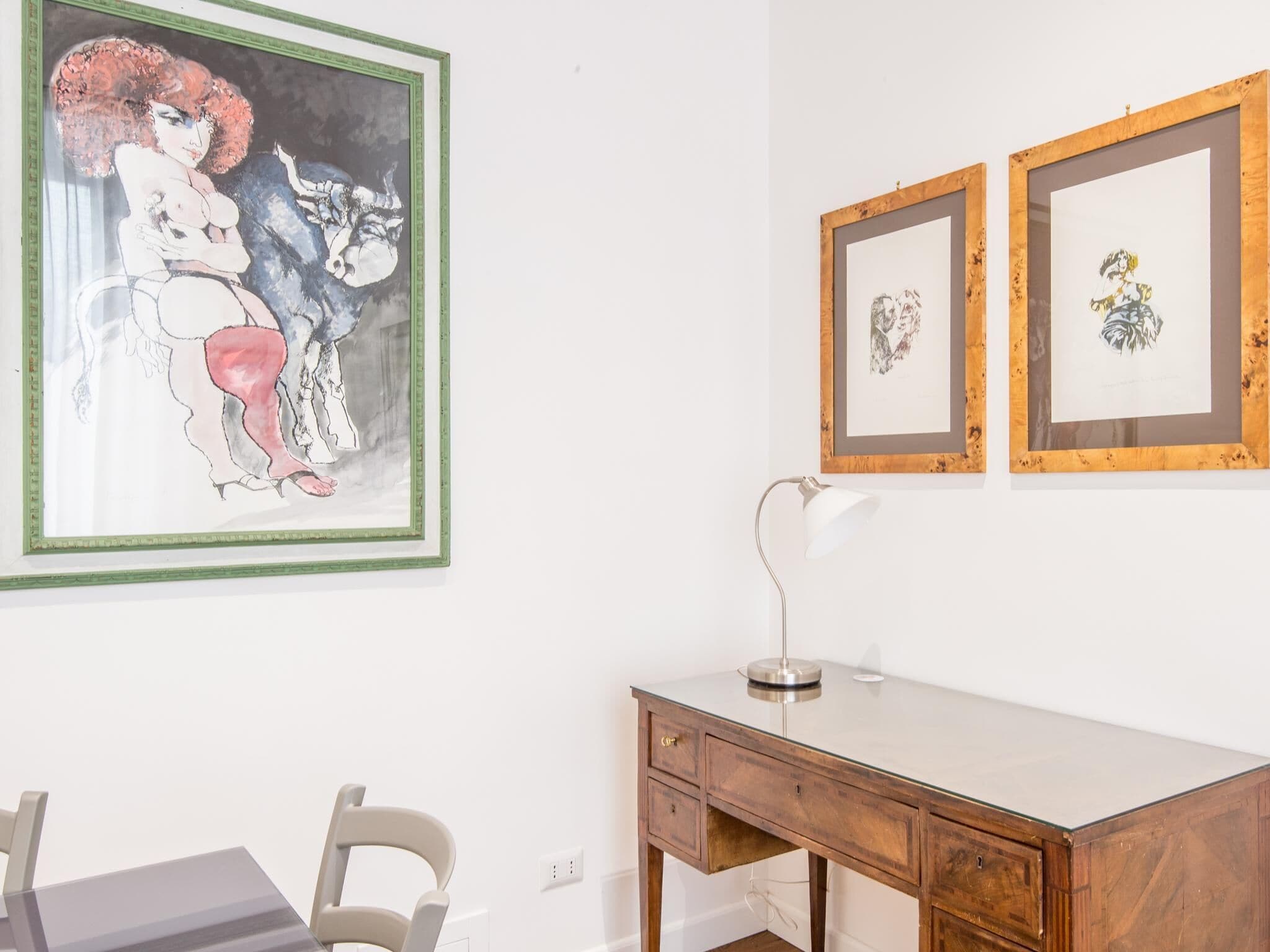 A room with a desk, a chair, and three framed artworks on the wall.