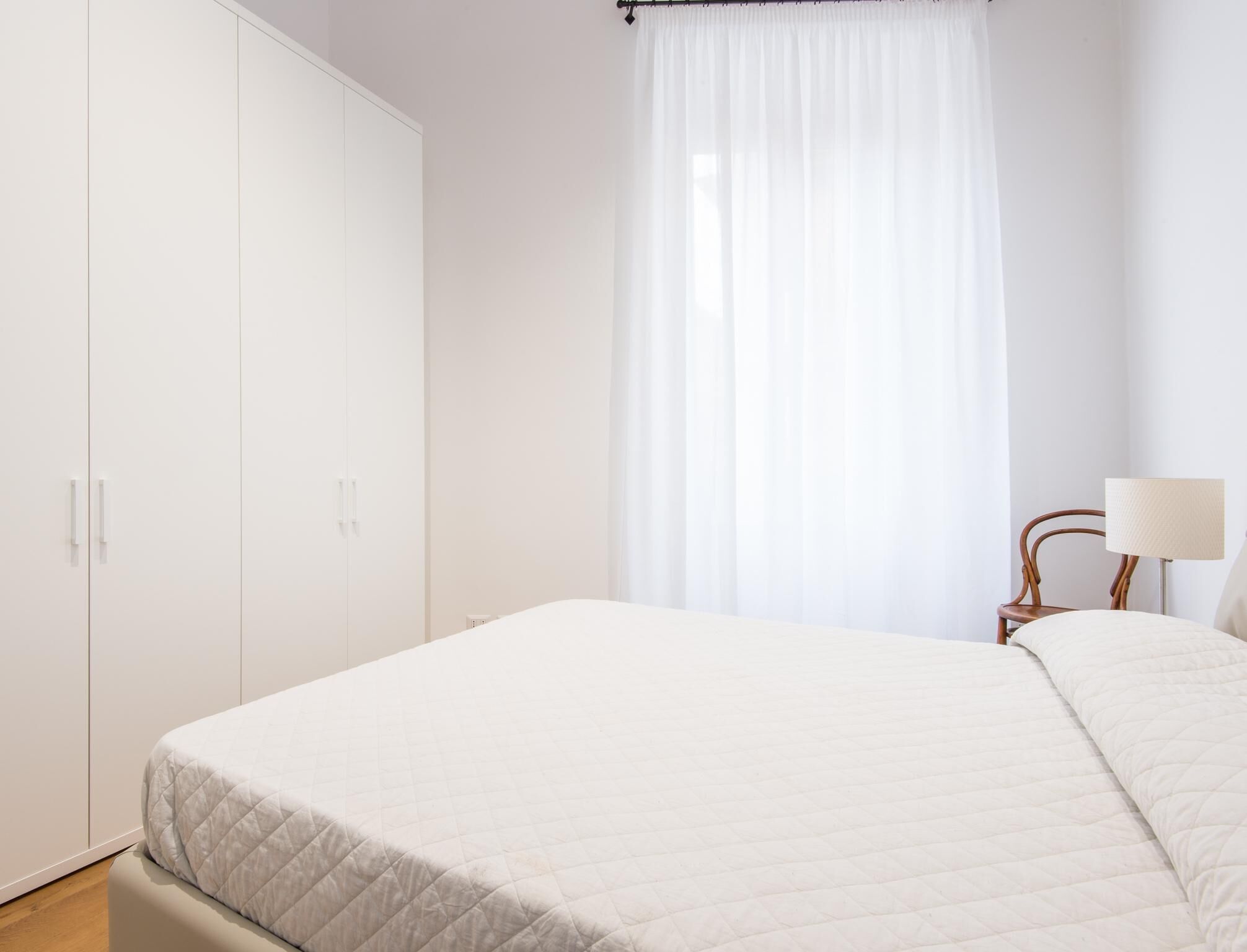 A bedroom with a bed, a wardrobe, a chair, and a lamp.
