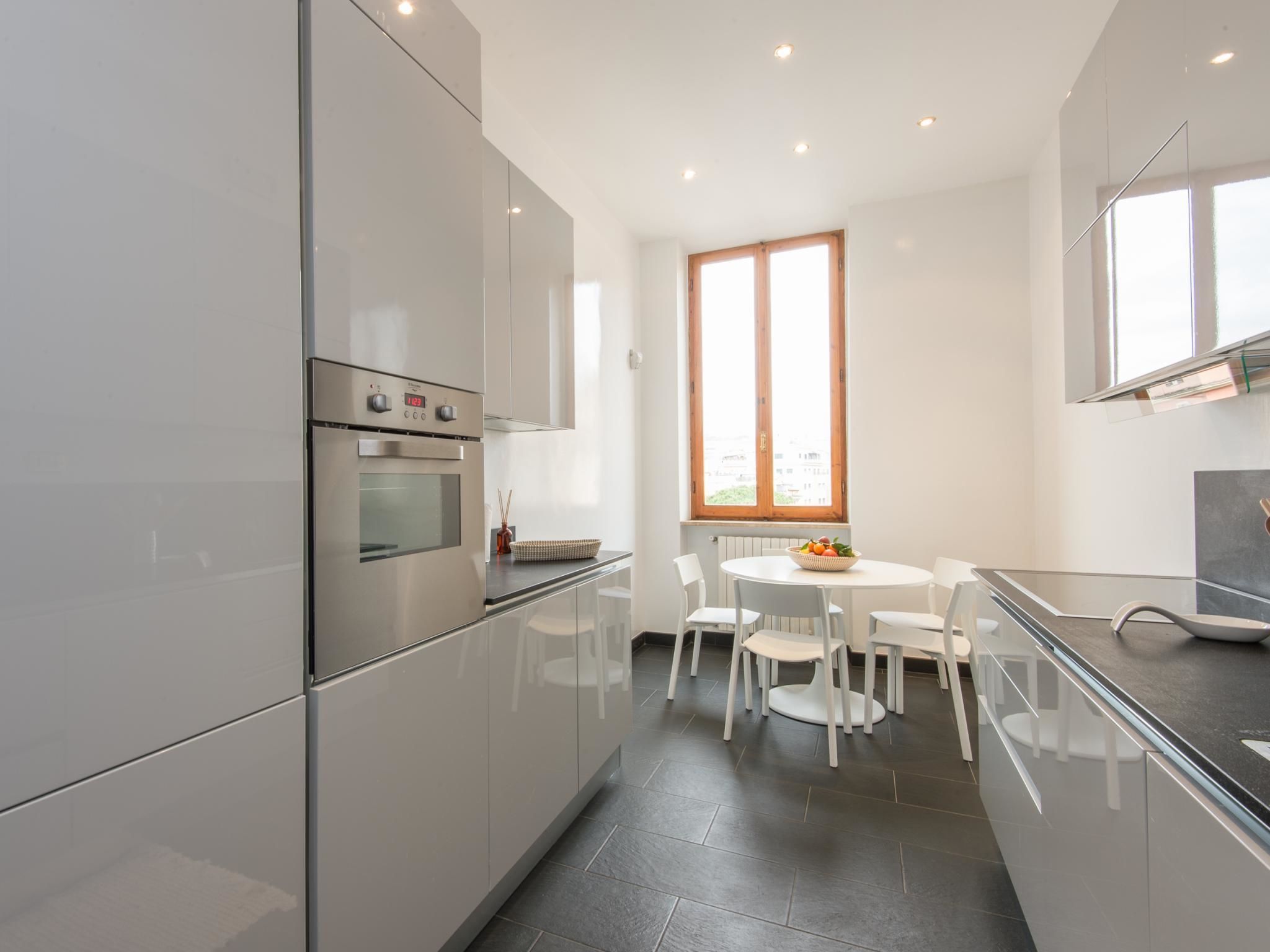 A modern kitchen with a built-in oven, a dining table with chairs, and a window providing natural light.