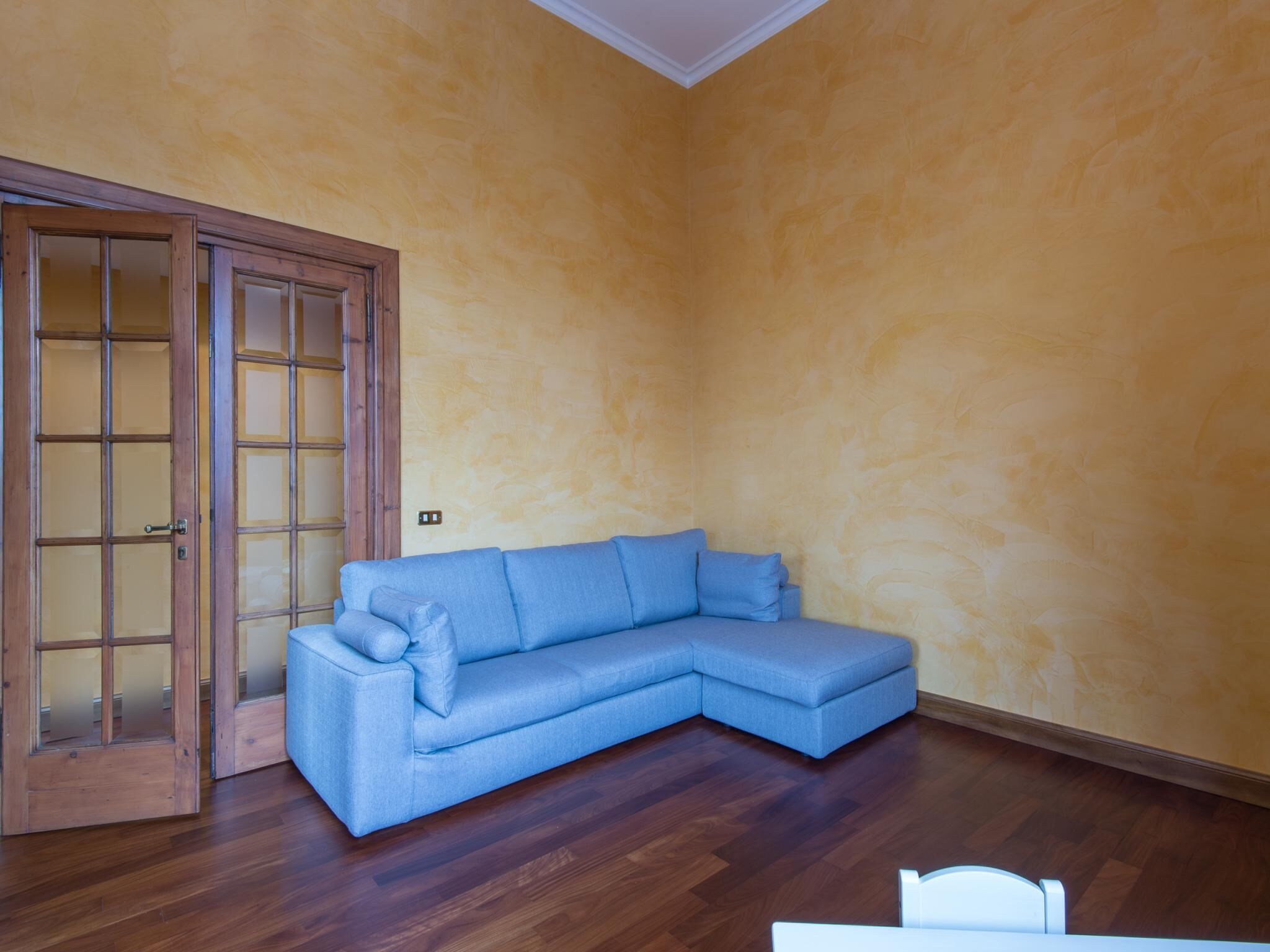 Une pièce avec un plancher en bois, un canapé d’angle bleu et une porte en bois dotée de panneaux de verre.