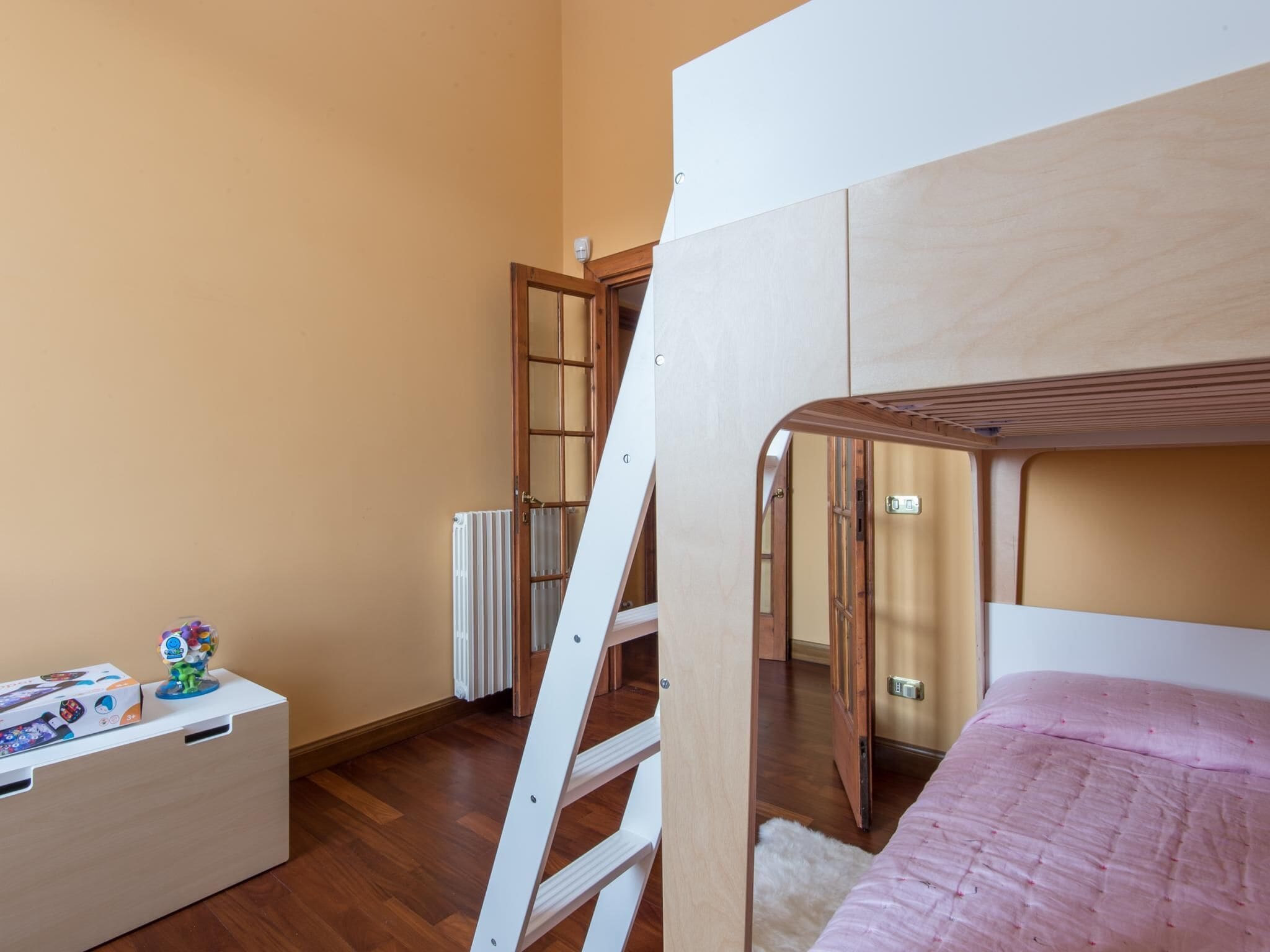 A bedroom with a bunk bed, a radiator, a white dresser, and a toy on the dresser.