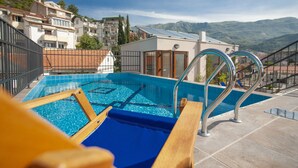 A rooftop pool with clear blue water, surrounded by a metal fence and wooden loungers. - Twelve by Aycon (Budva)