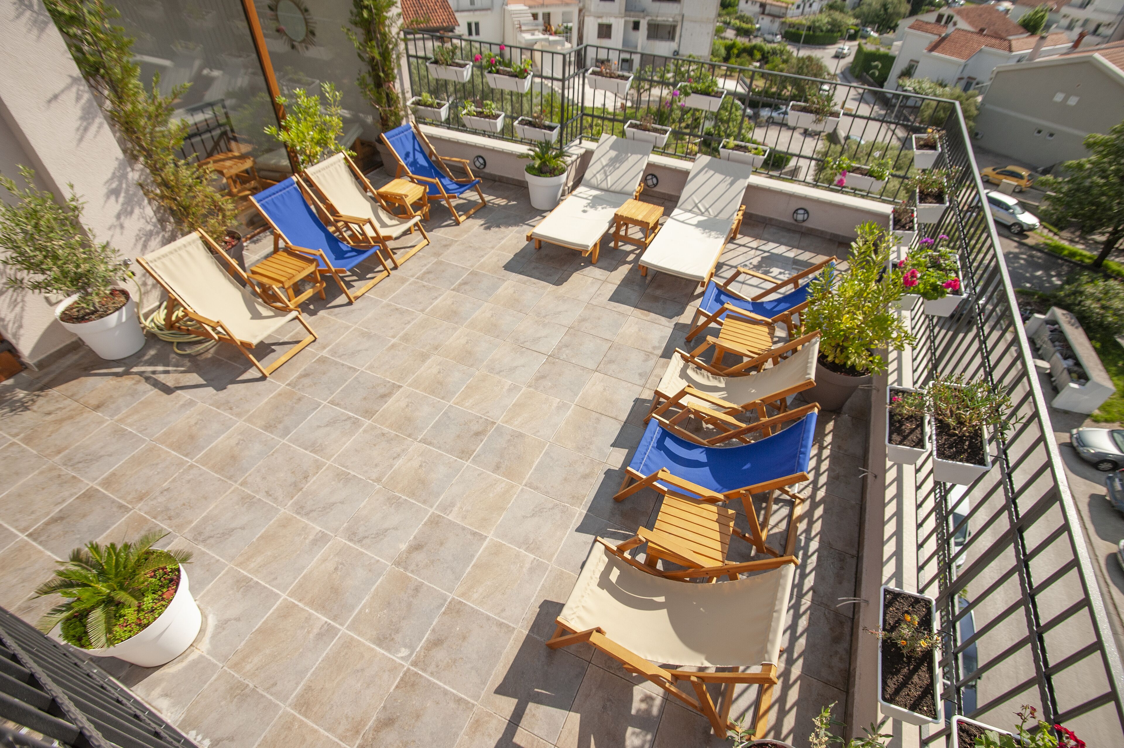 Una terraza en la azotea con sillones y mesas, rodeada de plantas en macetas y vistas panorámicas de la ciudad.