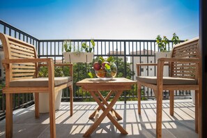 A wooden balcony with two chairs and a table, a potted plant, and a bowl of fruit. - Twelve by Aycon (Budva)