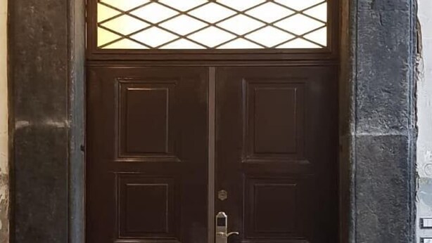 Une porte à deux battants en bois sombre, dotée d’une poignée en métal, encadrée par un cadre en pierre.