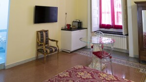 Une pièce avec un plafond orné de motifs, un téléviseur fixé au mur, une fenêtre avec des rideaux rouges, une chaise en bois, une table en verre et un tapis à motifs.