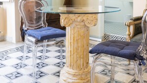 Une pièce comprenant une table à plateau en verre, deux chaises transparentes, un meuble en bois et un miroir.