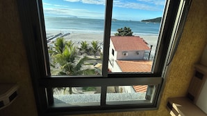 Une vue depuis une fenêtre donnant sur une plage, avec un bâtiment au premier plan.