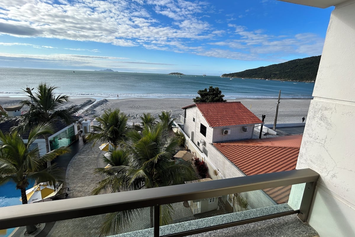 A balcony with a view of a beach, palm trees, and a building with a red roof.