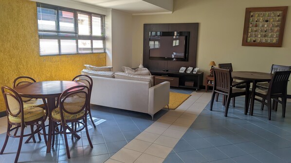 A living room with a sofa, dining table, chairs, a TV, and a framed picture on the wall. - GOLFINHOS APART HOTEL (Florianópolis)