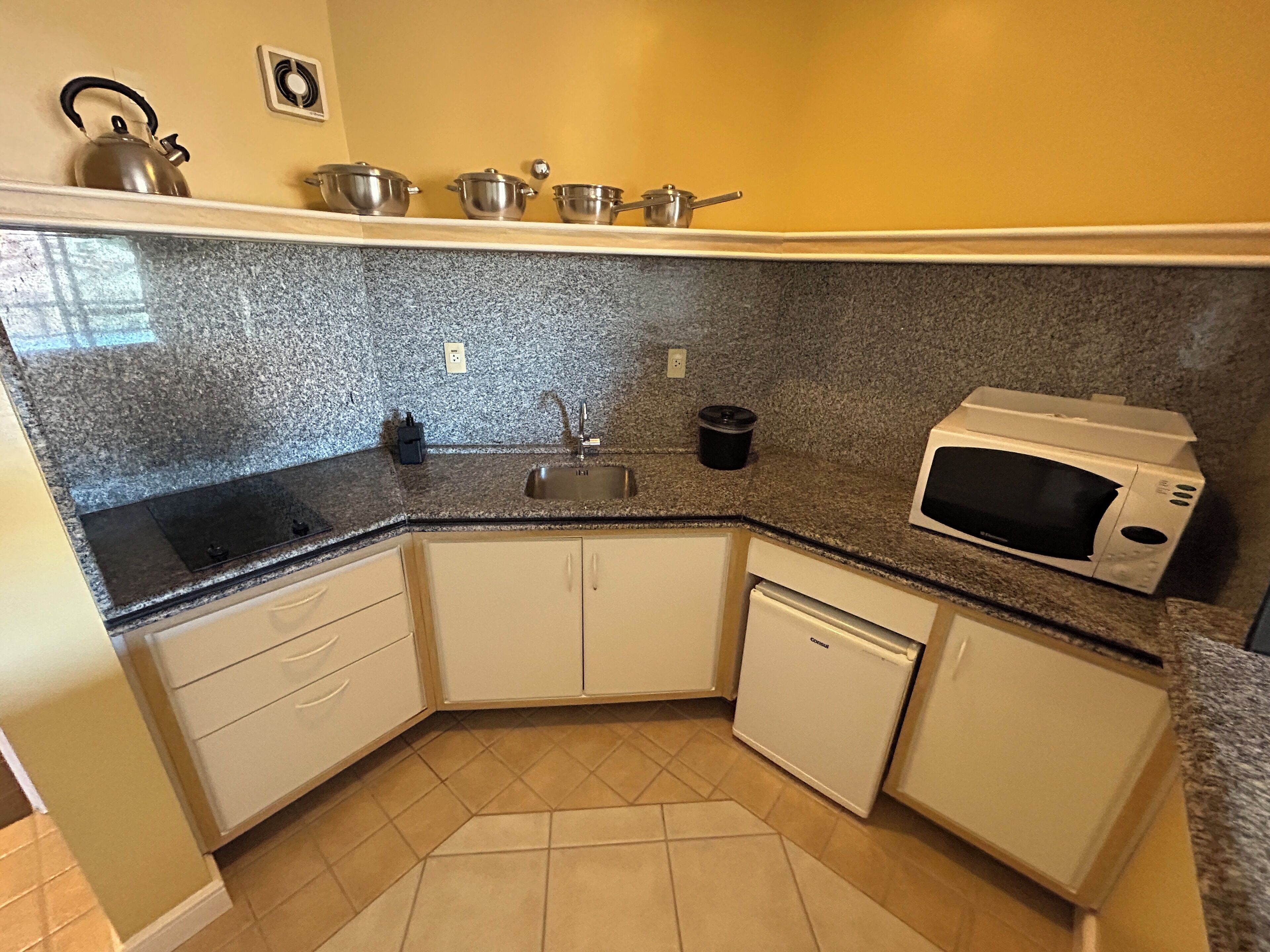 A compact kitchen with a granite countertop, a built-in sink, a microwave, and a compact refrigerator.