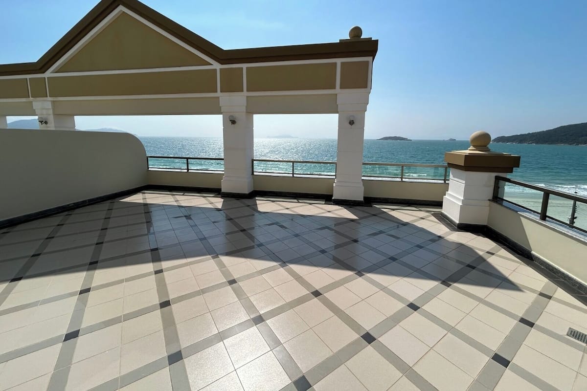 A covered terrace with a tiled floor, a view of the sea, and a building with a gabled roof.