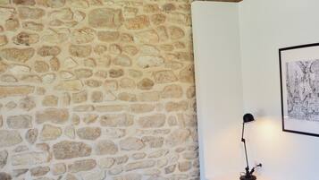A room with a stone wall, a gray sofa with a black pillow, a black floor lamp, and a black chair with a wireframe backrest.