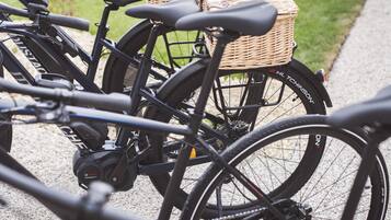 A row of bicycles parked on a gravel path with wicker baskets attached to the back.