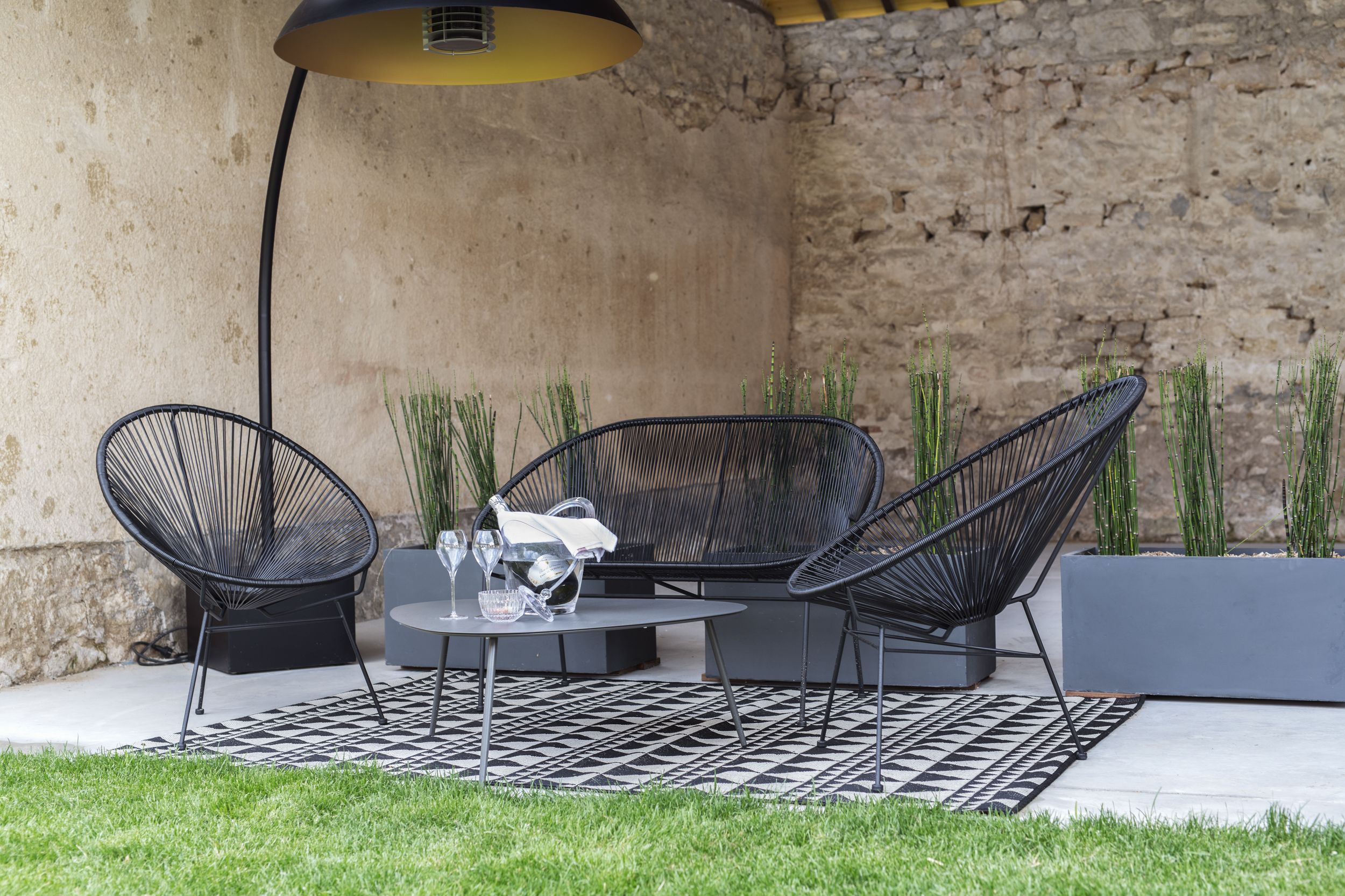 An outdoor seating area with two black wire mesh chairs, a round table, and a black and white patterned rug.