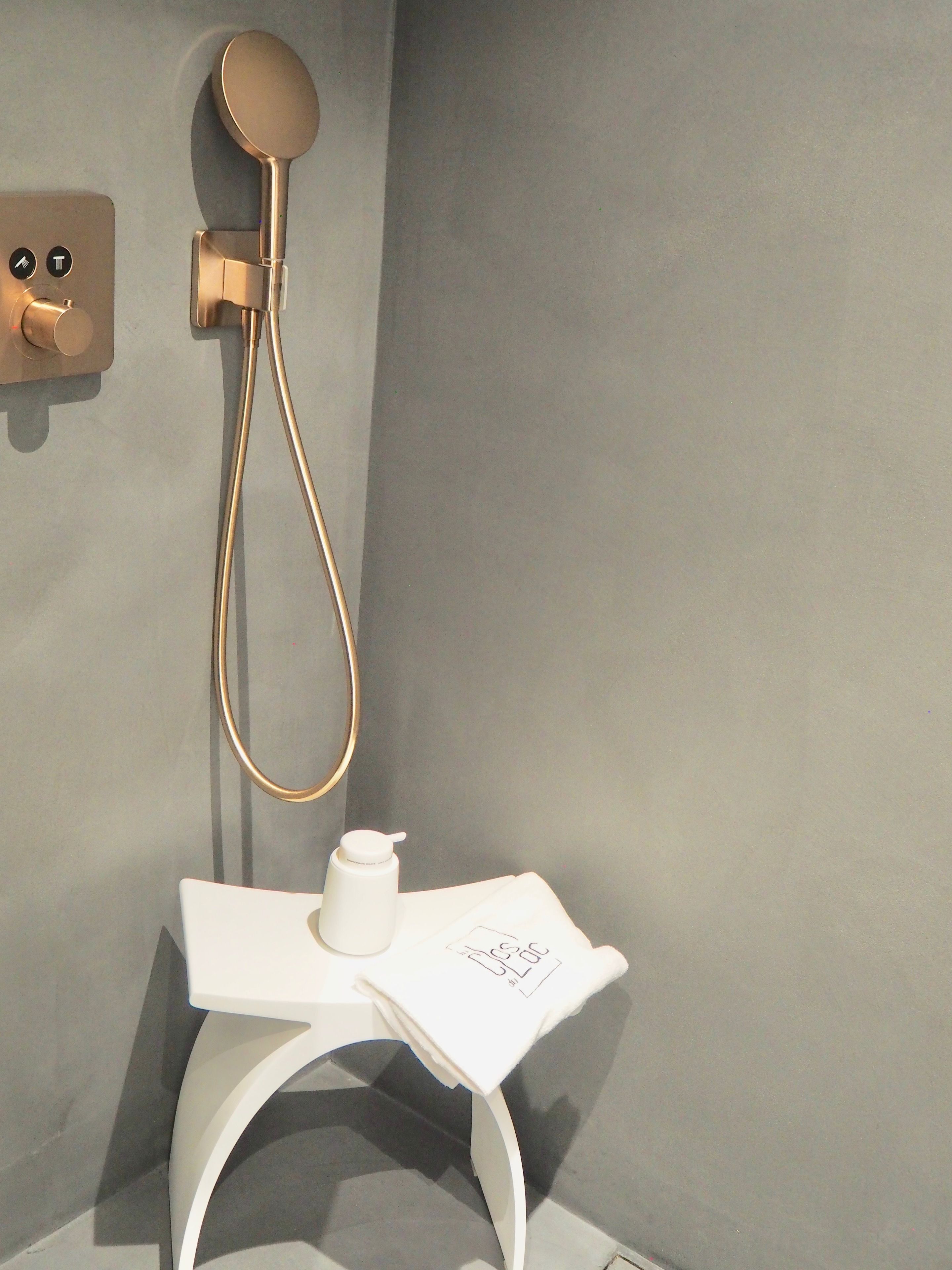 Un ba ño moderno con ducha de oro, un lavabo blanco y un pequeño recipiente blanco en la encimera.