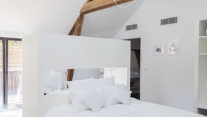 Une chambre moderne avec un lit blanc, des poutres en bois et une grande fenêtre.
