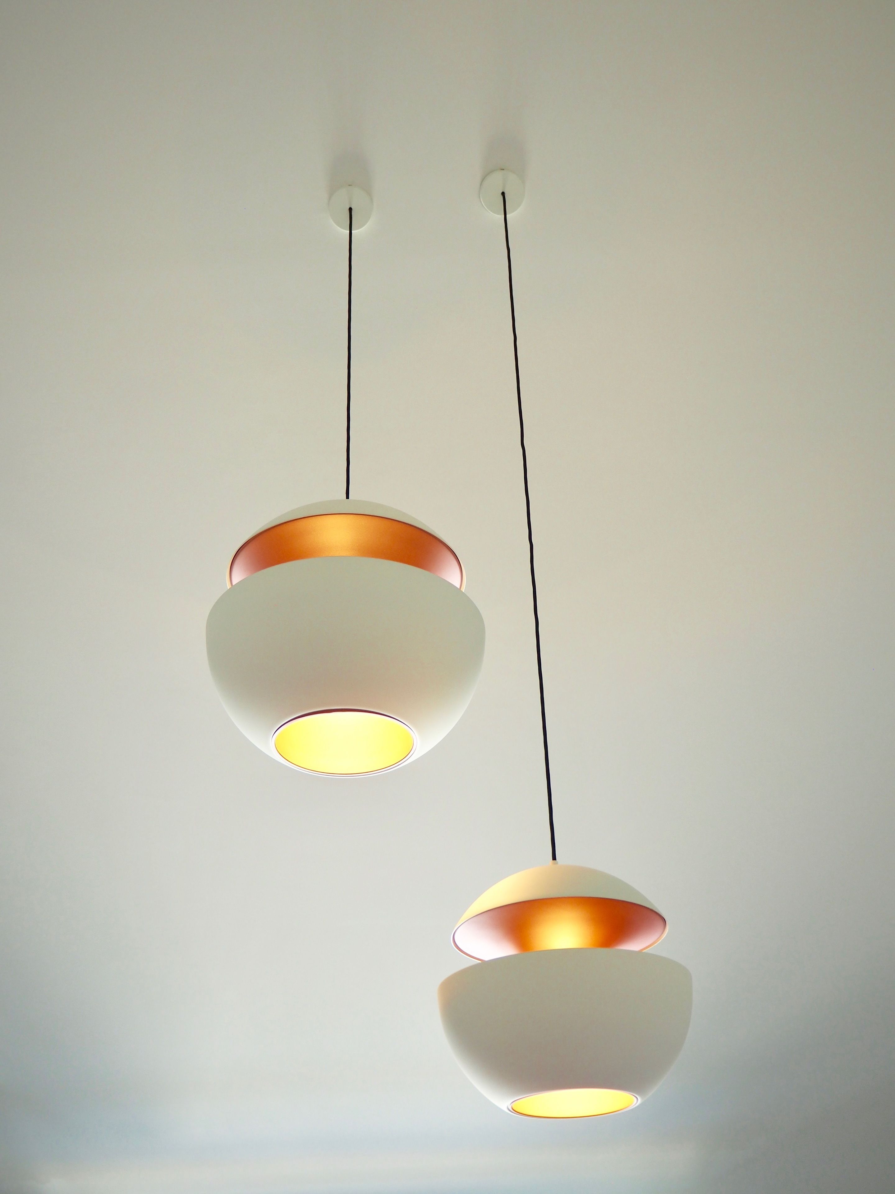 Two pendant lights with a white and copper design against a plain wall.