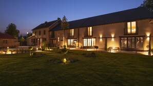 Une maison moderne dotée d’un patio bien éclairé, de grandes fenêtres et d’une vaste pelouse.