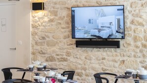 Un espace de restauration moderne avec des murs en pierre, un téléviseur fixé au mur et des chaises noires.