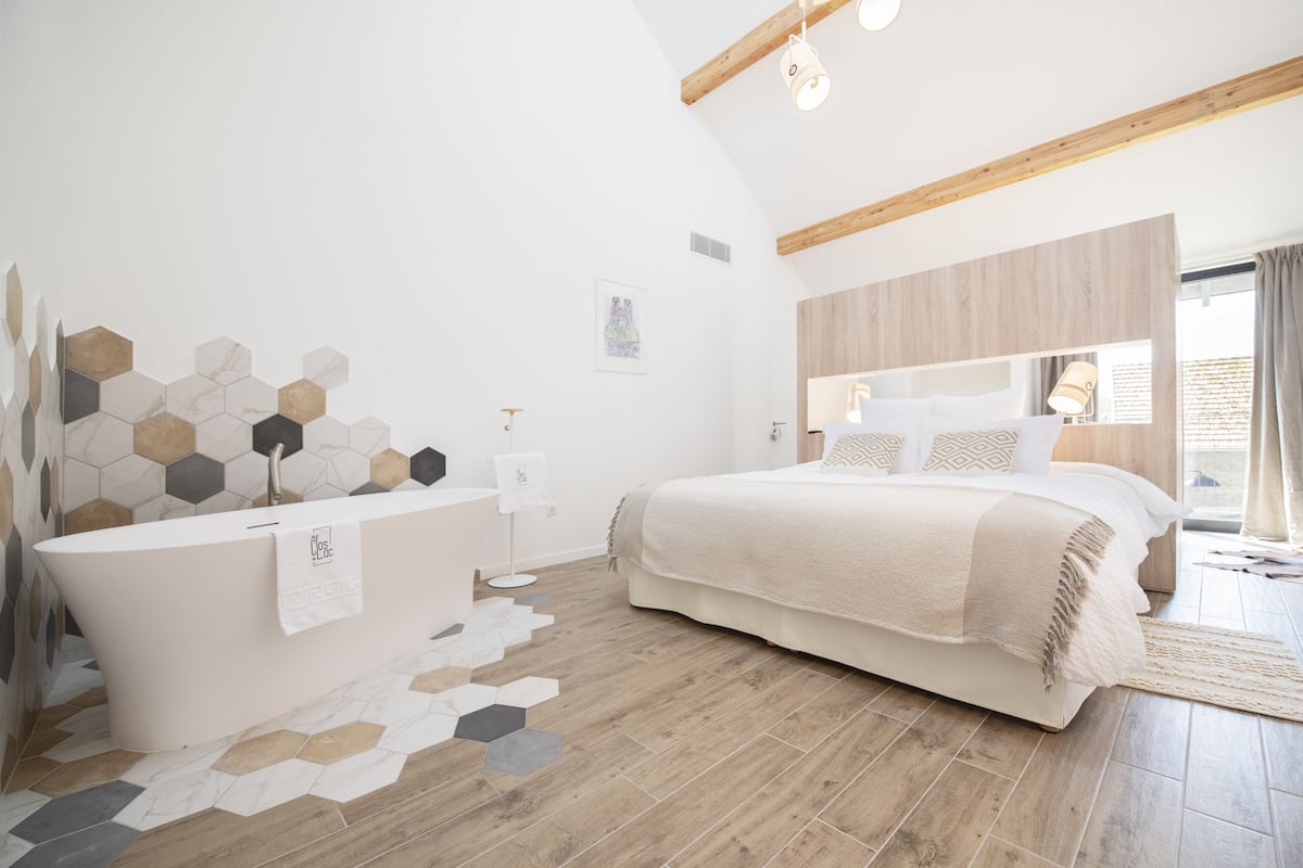 Quarto moderno com uma cama grande, uma banheira independente e teto de madeira.
