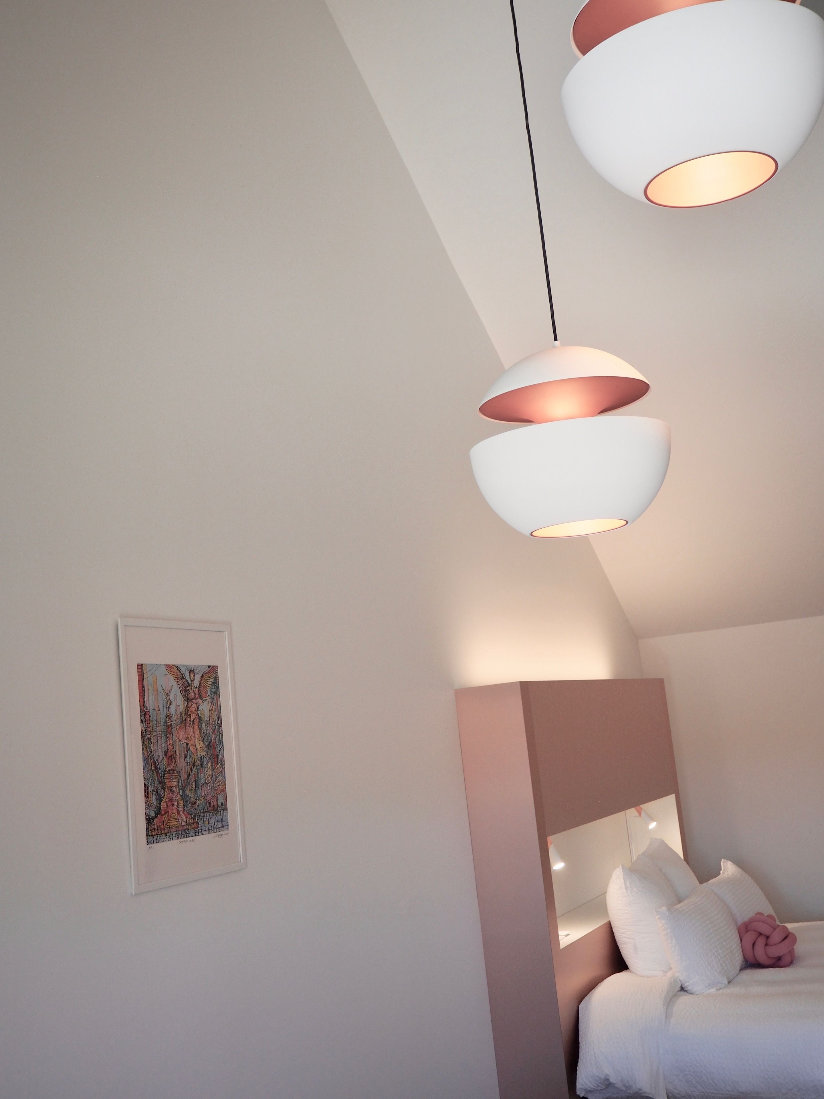 A bedroom with a bed, white bedding, a pink decorative pillow, and a framed artwork on the wall.