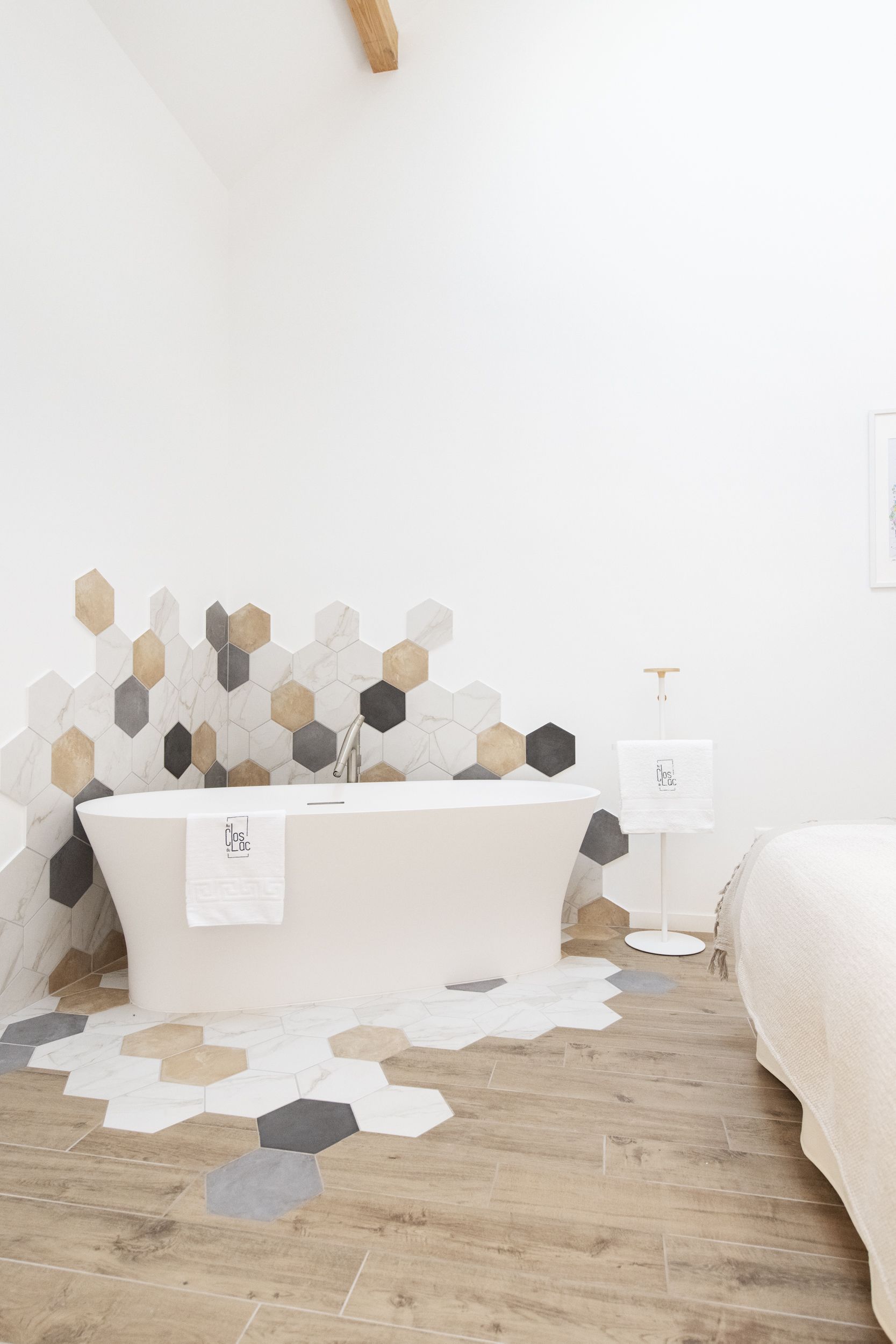 A modern bathroom with a freestanding bathtub, hexagonal tile backsplash, and a wooden floor.