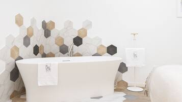 A modern bathroom with a freestanding bathtub, hexagonal tile backsplash, and a wooden floor.