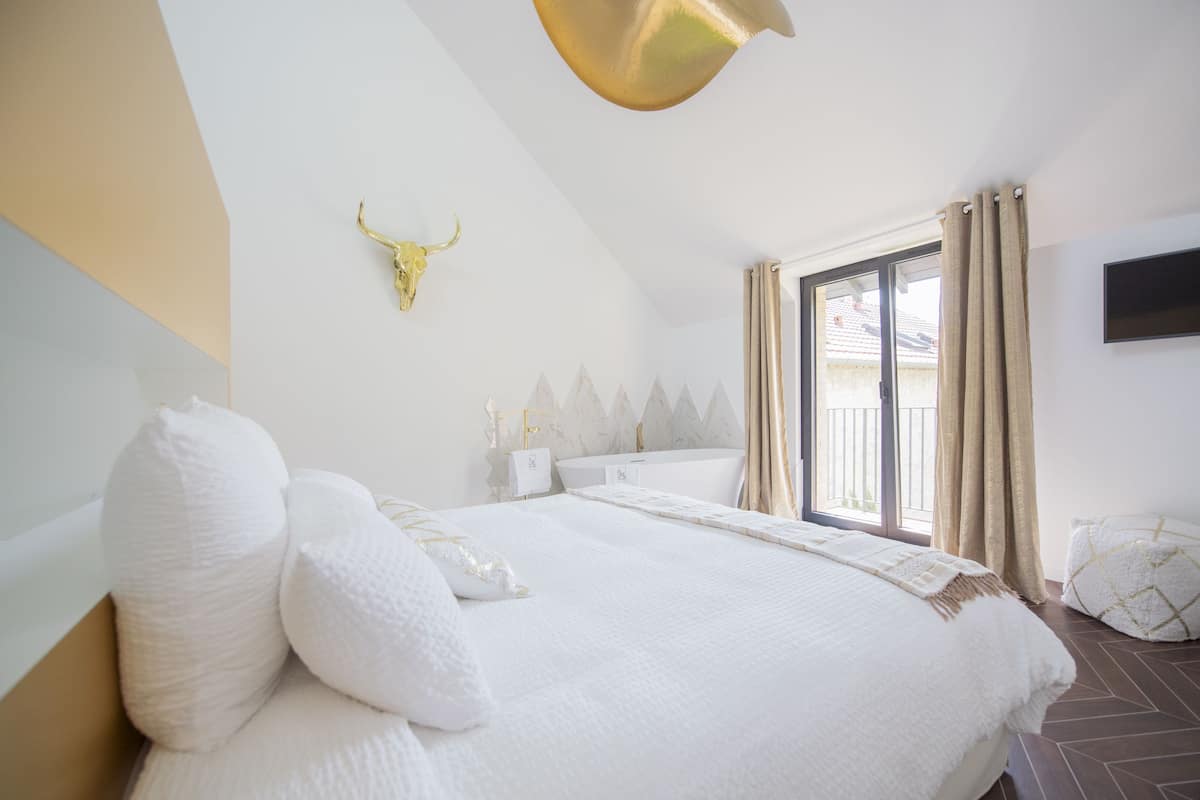 Quarto com uma cama grande, decoração dourada na parede, banheiro com banheira e janela com cortinas.