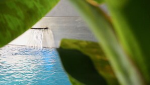 Un élément décoratif aquatique comprenant un bassin à l’eau claire et bleue ainsi qu’une cascade.