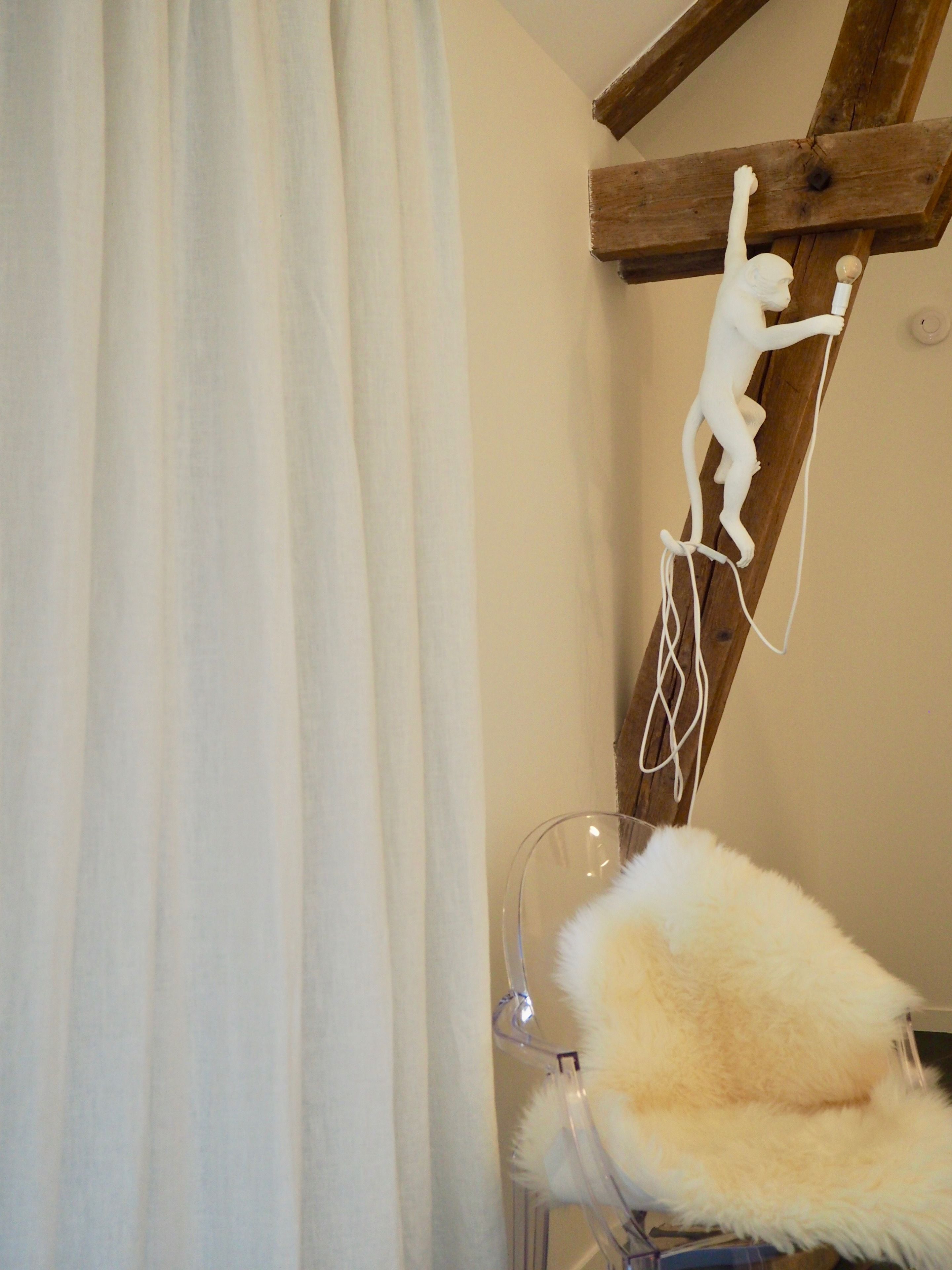 A room with a wooden beam structure, a white sculpture, a fur chair, and a clear glass object.