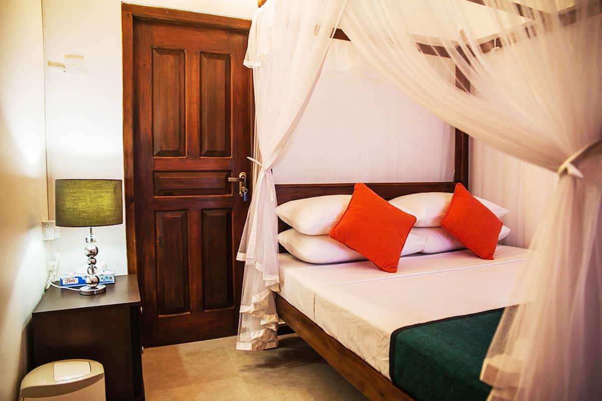 Une chambre avec une porte en bois, une table de chevet avec une lampe et un lit avec des oreillers blancs et rouges.