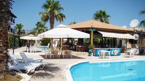 Zona de piscina con sillones de descanso, sombrillas y un bar.