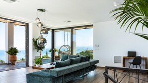 A modern living room with a large sofa, a dining area, and a view of the sea. - Villa Blue Skyline (Apokoronas)