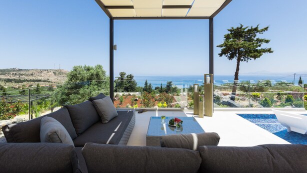 A modern outdoor seating area with a sofa and a table, overlooking a scenic landscape with a pool and a view of the sea. - Villa Blue Skyline (Apokoronas)