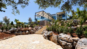 A modern building with a glass facade, stone pathway, and a rock garden. - Villa Blue Skyline (Apokoronas)