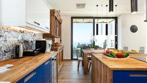 A modern kitchen with wooden cabinets, a blue countertop, and a view to the outside. - Villa Blue Skyline (Apokoronas)