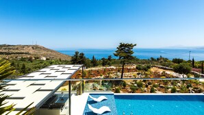 A modern pool area with clear blue water, a glass balustrade, and a view of the sea and hills. - Villa Blue Skyline (Apokoronas)