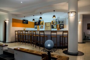 Zona de bar con sillas de madera y una barra central, rodeada de estanterías llenas de botellas.