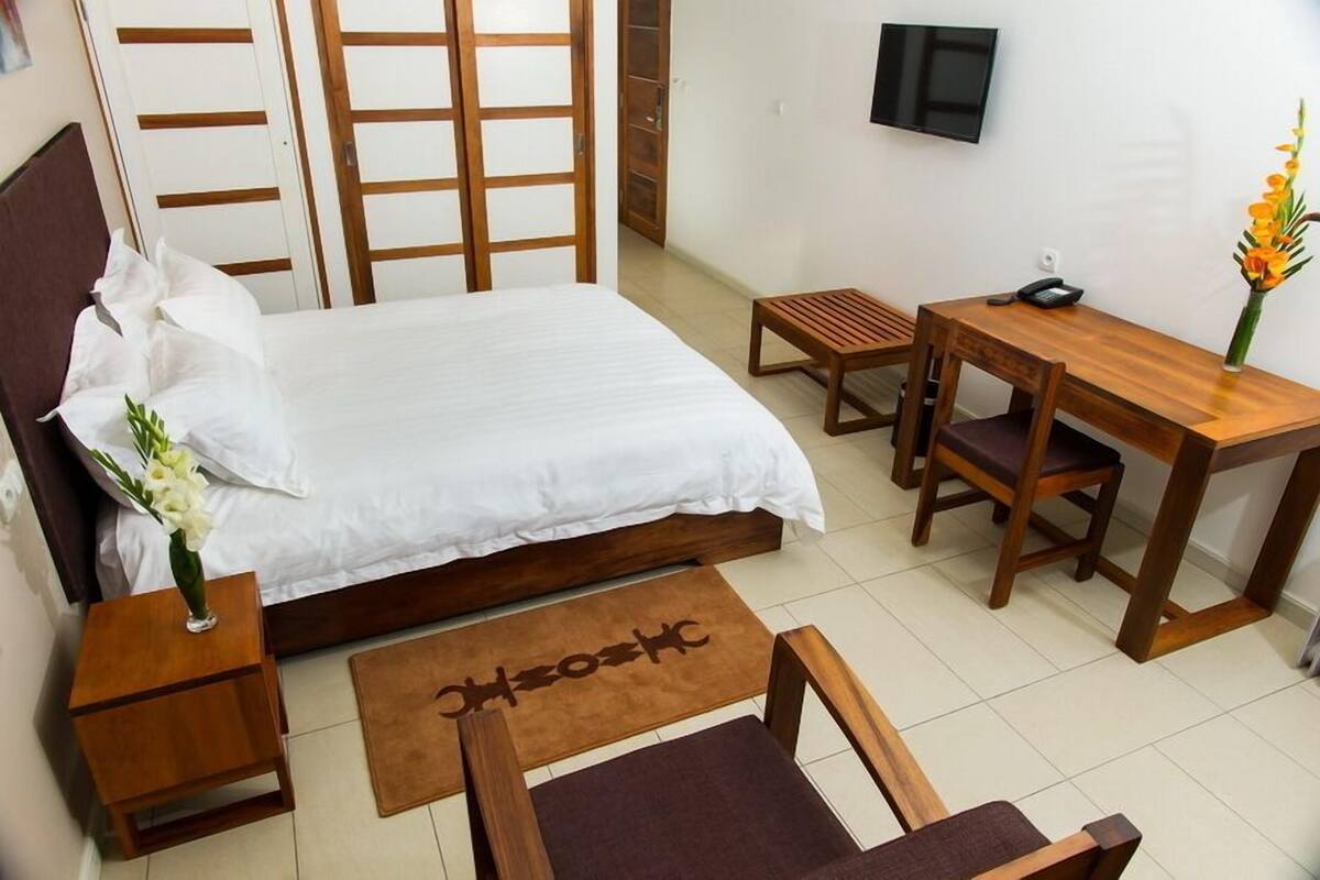 A bedroom with a bed, bedside tables, a desk, a chair, a TV, and a small table with a vase of flowers.