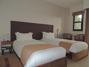 A hotel room with two beds, a nightstand, a window with curtains, and a small table with a vase of flowers.