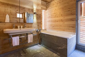 A wooden-paneled bathroom with a large sink, mirror, and bathtub. - Alpenlofts (Bad Gastein)